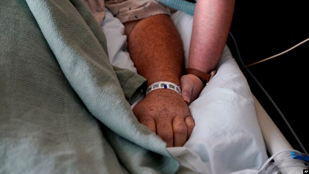 FILE - A woman, who is on oxygen as she recovers from COVID-19, holds the hand of her husband, who also contracted COVID-19, as he is kept alive with the help of an oxygenation machine at a medical center in Shreveport, La., Aug. 18, 2021.