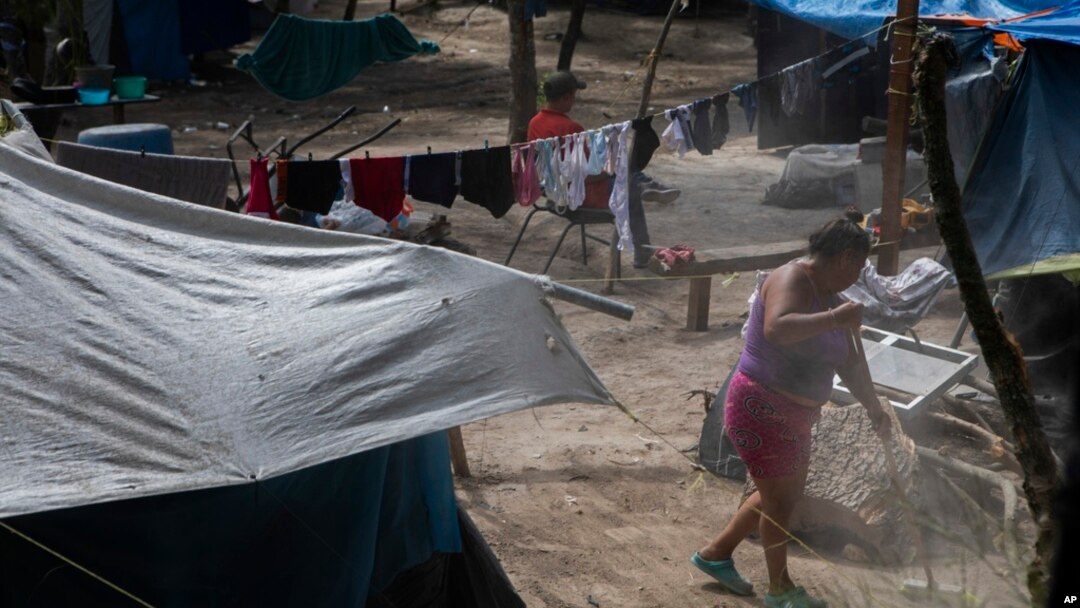 A migrant sweeps the ground at a shelter encampment in the border town of Matamoros, Mexico, Aug. 16, 2023. 