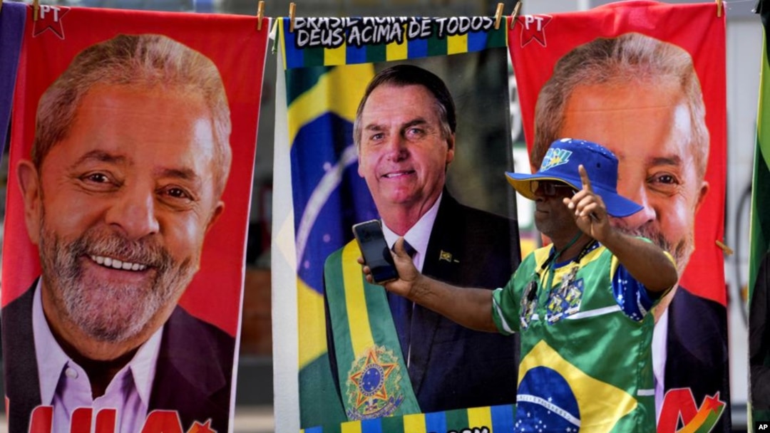 Un manifestante vestido con los colores de la bandera brasileña camina frente a unas toallas de un vendedor ambulante que muestran a los candidatos presidenciales brasileños, en Brasilia, el martes 27 de septiembre de 2022. (AP Foto/Eraldo Peres)