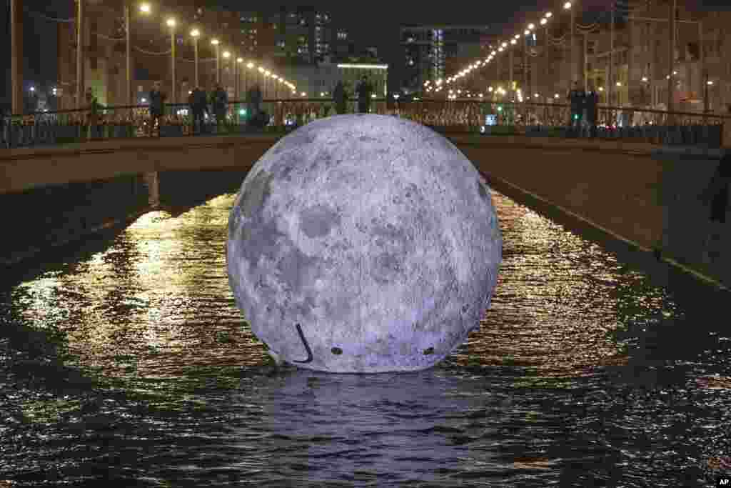 People look at a giant floating ball depicting the moon's surface, an installation for the "Festival of Lights," in the water of Obvodny channel in St. Petersburg, Russia, Nov. 3, 2018.