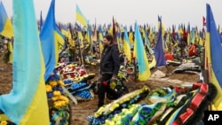 A man carries flowers to lay at the grave of a killed soldier in a city cemetery in Kharkiv, Ukraine, March 21, 2023.