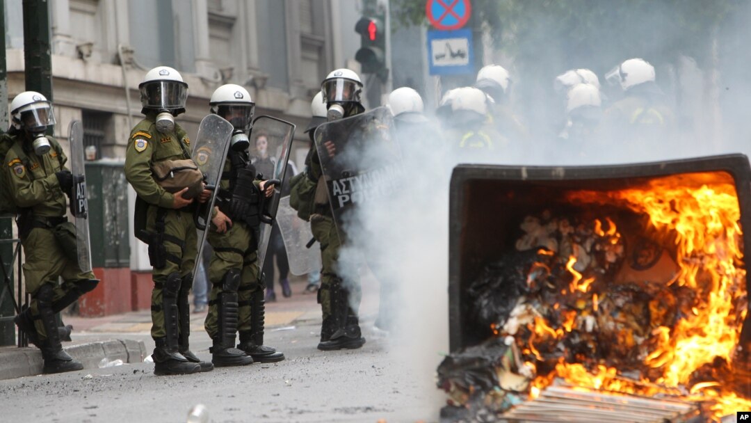 A fire burns as riot police look on during clashes with activists protesting German Chancellor Angela Merkel's visit in Athens, Greece, Oct. 9, 2012. 