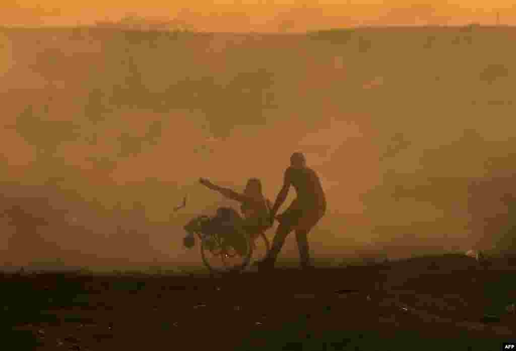 A Palestinian protester pulls a fellow protester on wheelchair amid clouds of tear gas fired by Israeli forces during clashes in east of Gaza City near the Israeli border.