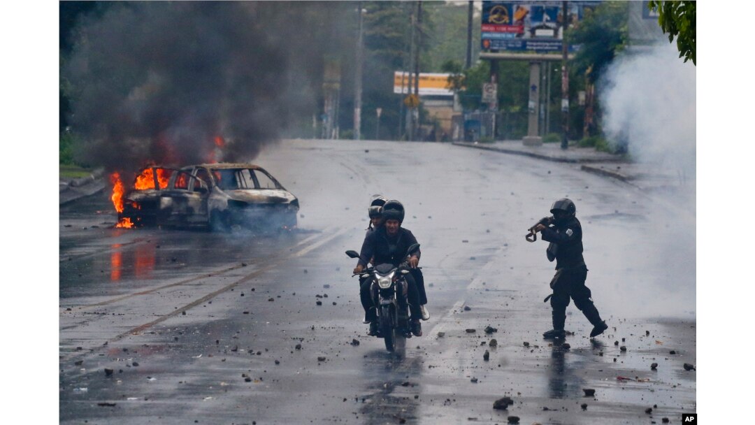 A police officer aims his shotgun at two men riding a motorcycle during a protest against Nicaragua's President Daniel Ortega in Managua, May 28, 2018.