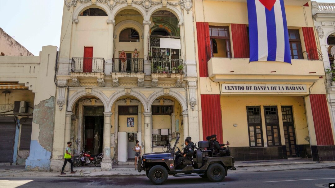 FILE - Special forces police patrol the streets as they drive past a large Cuban flag hanging from the facade of a building, in Havana, Cuba, July 21, 2021.