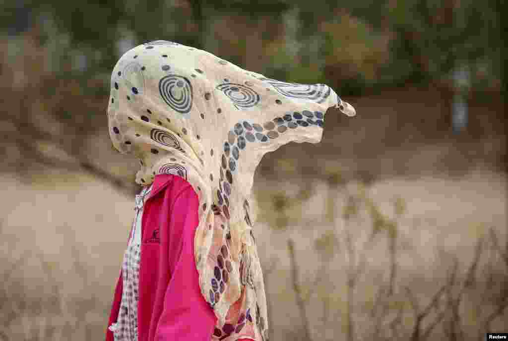 A woman protects herself from pollution by covering her face with a scarf, while walking in a park in Beijing, China.