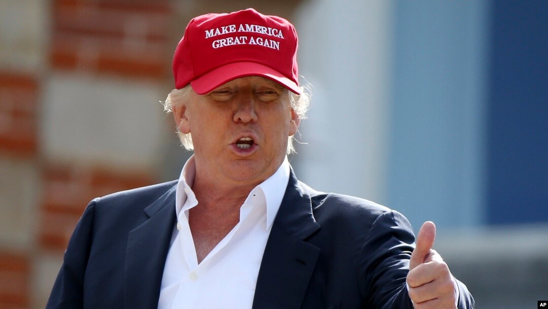 Donald Trump habla conlos periodistas luego de llegar en helicóptero al Abierto Británico de Golf, en Escocia. El letrero en su gorra lee: "Hagamos a Estados Unidos grande de nuevo".