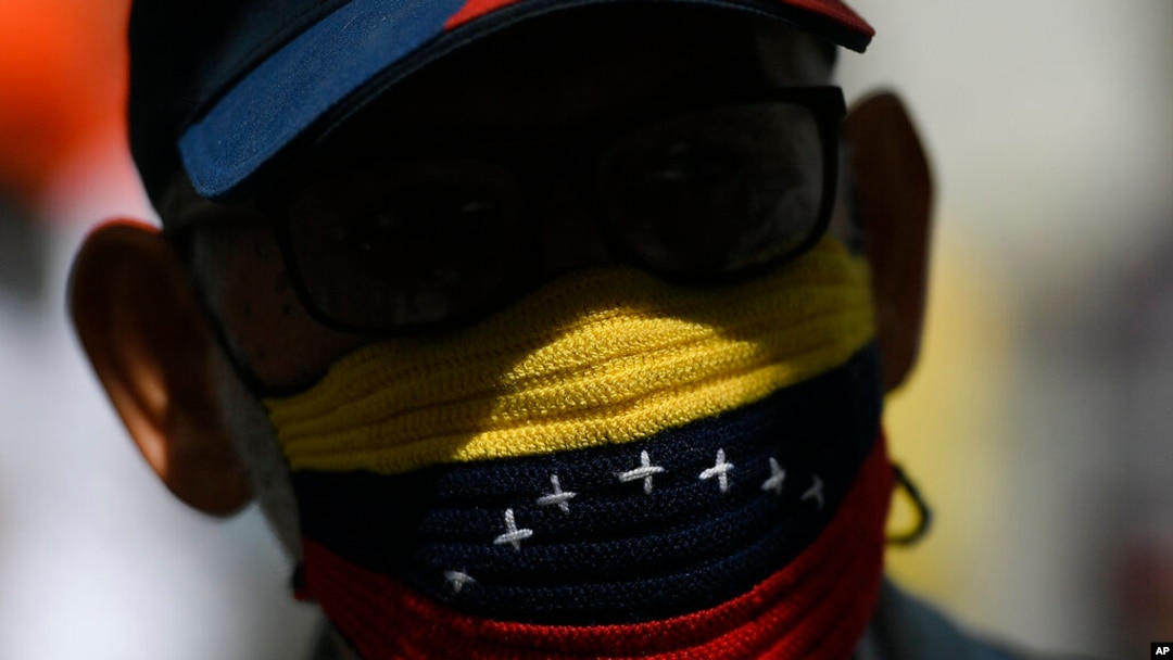 Un manifestante, con una mascarilla tejida a mano con los colores representativos de la bandera venezolana, asiste a una marcha exigiendo una distribución más equitativa y rápida de las vacunas contra el COVID-19 en Caracas, el 7 de abril de 2021.