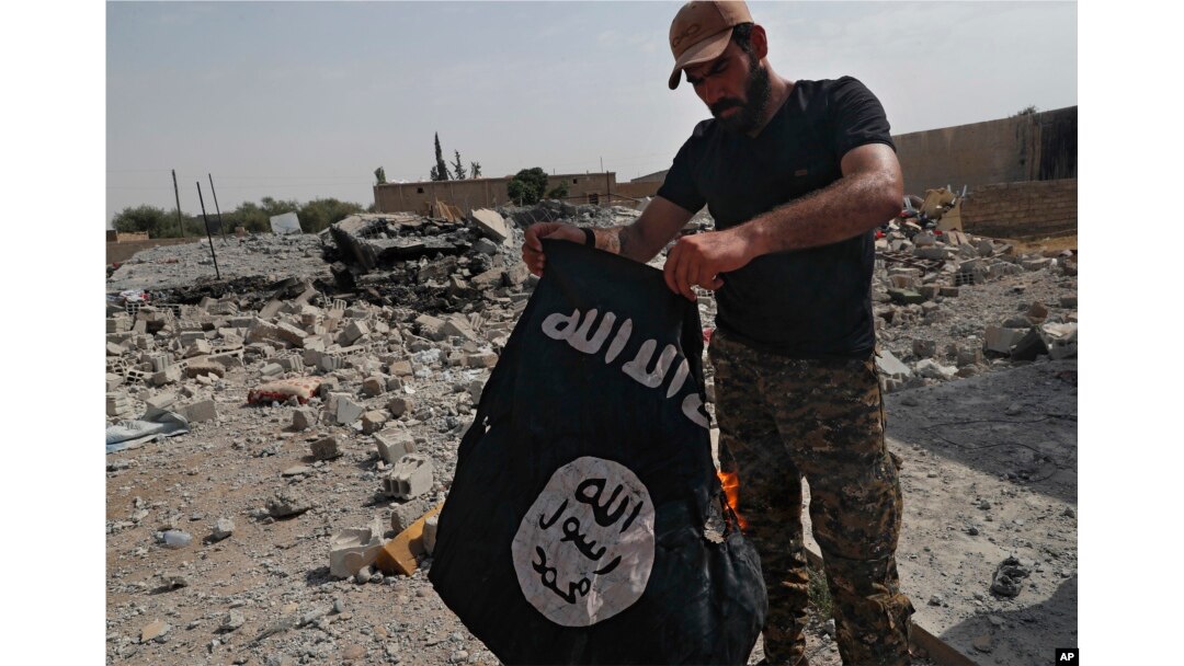 FILE - A fighter of the Christian Syriac militia burns an IS flag on the front line on the western side of Raqqa, northeast Syria, July 17, 2017.