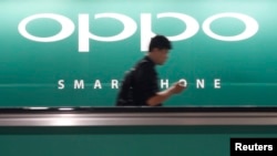 A commuter using his mobile phone passes an advertisement of Chinese smartphone maker Oppo at a train station in Singapore, May 8, 2014. 