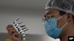 An employee inspects syringes of the SARS CoV-2 Vaccine for COVID-19 produced by SinoVac at its factory in Beijing, Sept. 24, 2020.