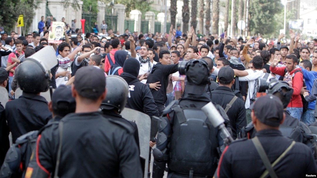 FILE - Cairo University students who support the Muslim Brotherhood and ousted Egyptian President Mohamed Morsi shout slogans against the military and Interior Ministry in front of riot police at the main gate of the university, Cairo, Nov. 24, 2013.