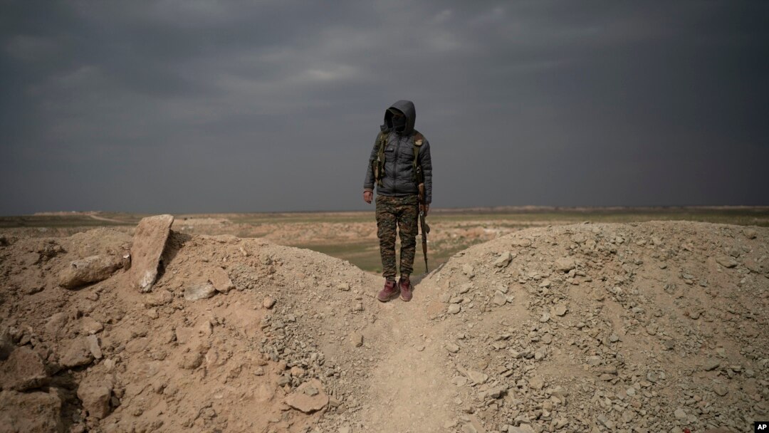 A U.S.-backed Syrian Democratic Forces (SDF) fighter stands atop a hill in the desert outside the village of Baghuz, Syria, Feb. 14, 2019. 