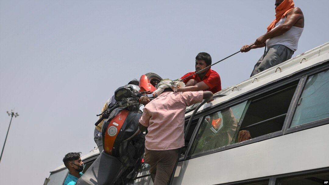 FILE - Indians load a motorcycle on the roof of a bus carrying migrant workers, who are leaving the capital during the COVID pandemic, in New Delhi, India, June 16, 2020.