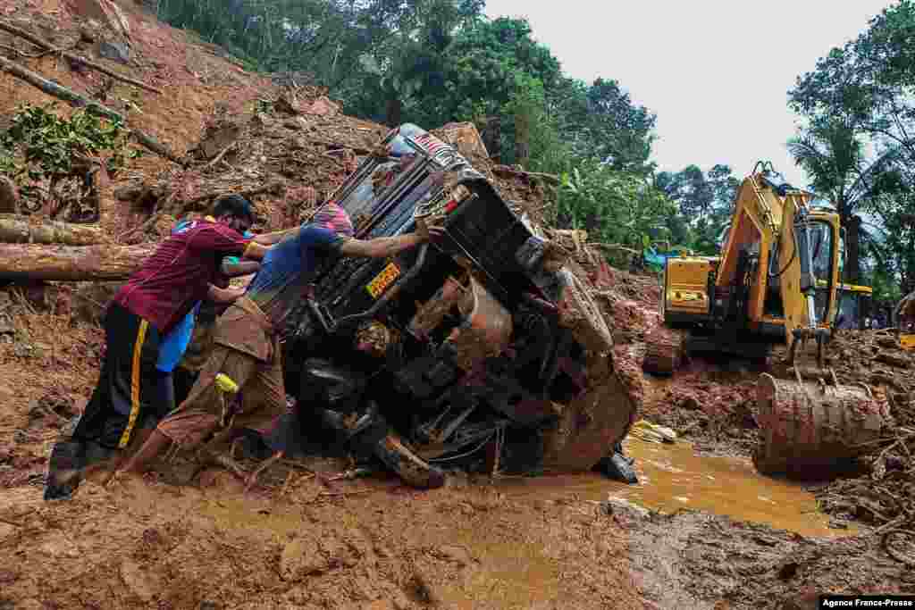 Rescue workers push a overturned vehicle stuck in the mud and debris at a site of a landslide caused by heavy rains in Kokkayar in India's Kerala state.