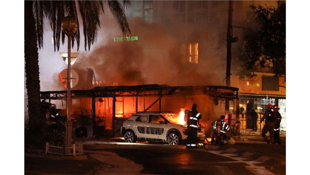 Israeli firefighters, security and rescue forces stand next to a burning bus and car that were hit by a rocket fired from Gaza towards Holon, Israel, May 11, 2021.
