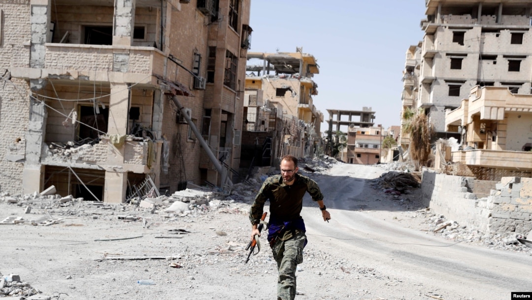 FILE - A British volunteer fighter of Syrian Democratic Forces runs for cover to avoid sniper fire of Islamic State militants, at the front line in Raqqa, Syria, Oct. 7, 2017. 